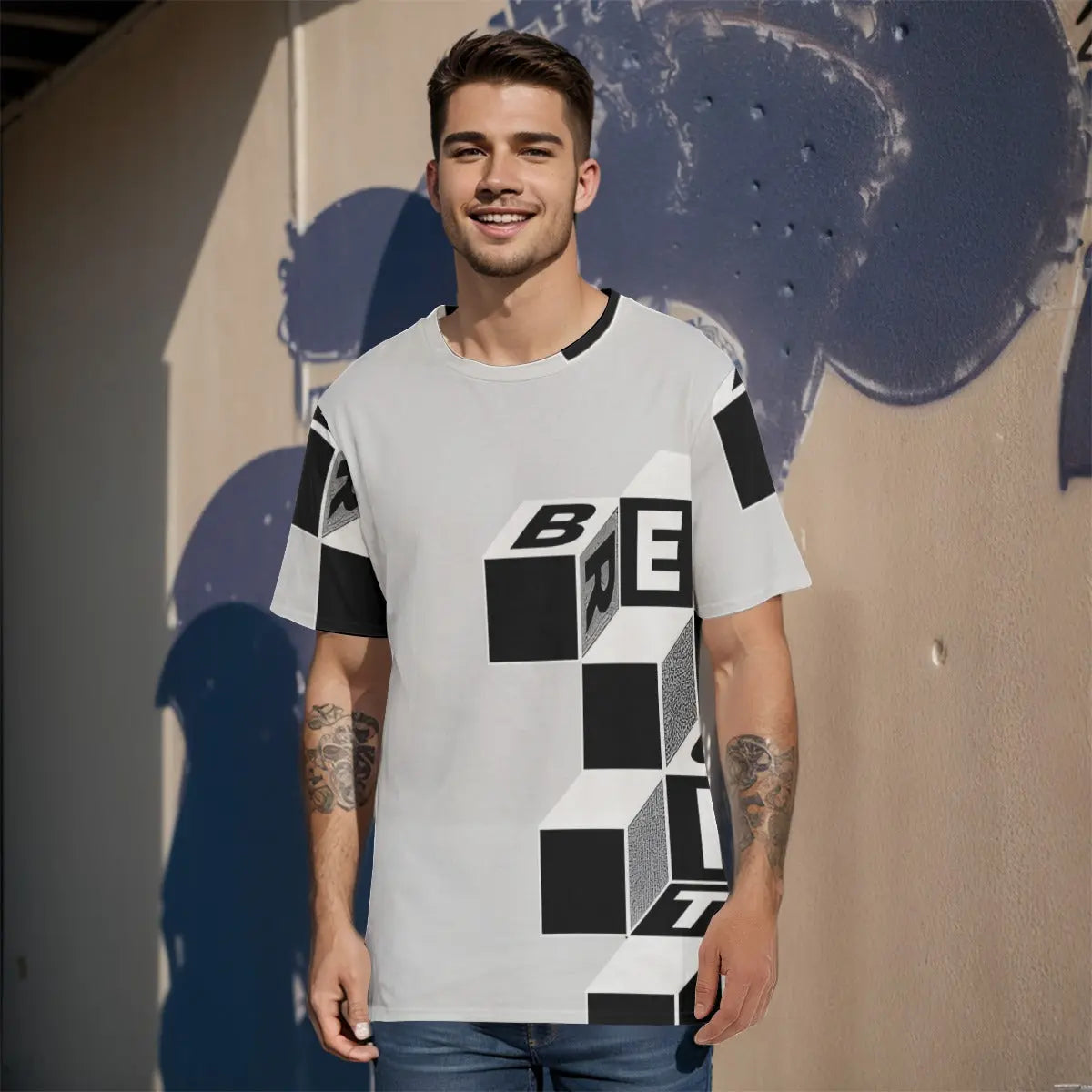 Young man wearing graphic cotton T-shirt with geometric cube design, standing against a textured wall in casual sunlight.