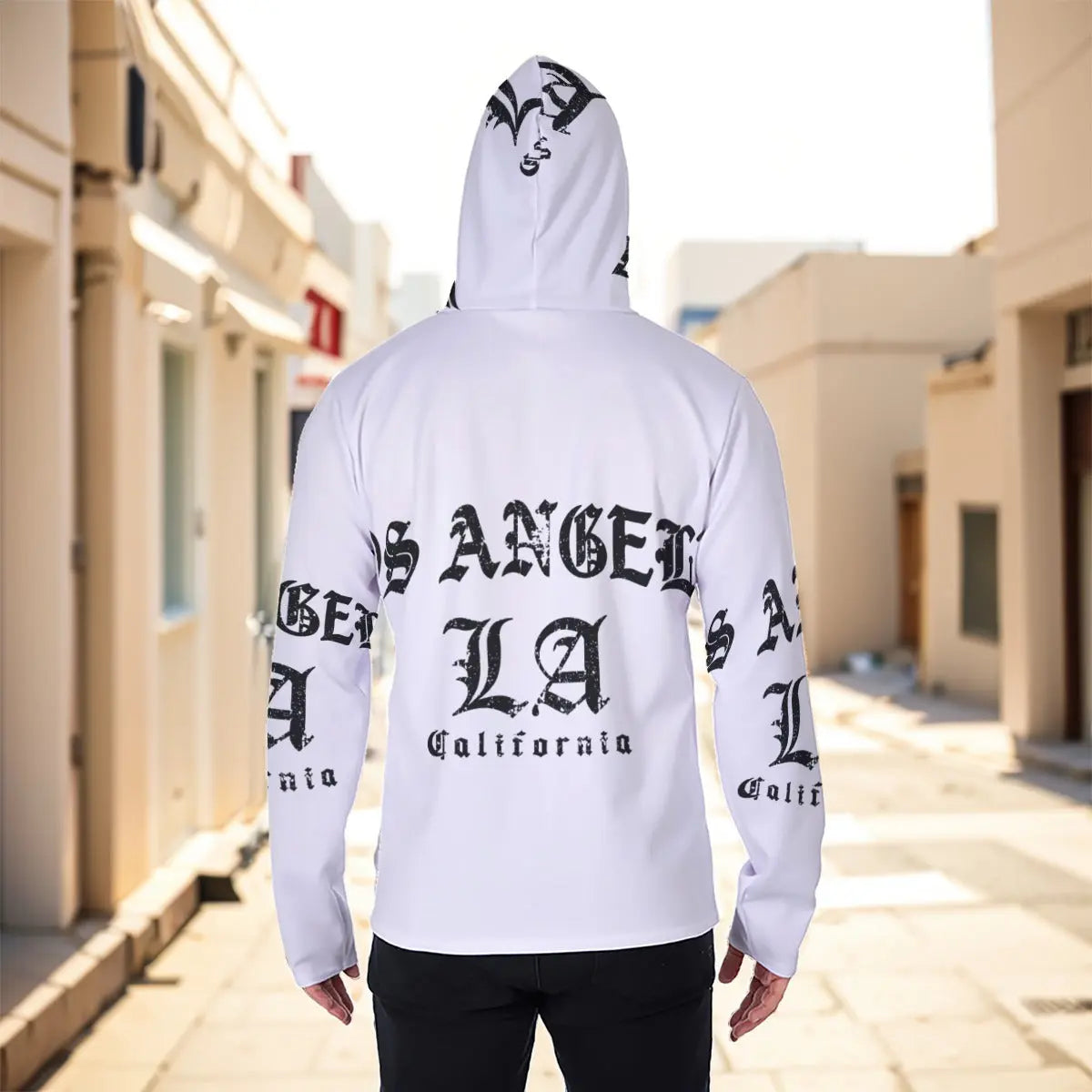 Back view of man wearing white hoodie with black Los Angeles print, standing in urban alleyway.