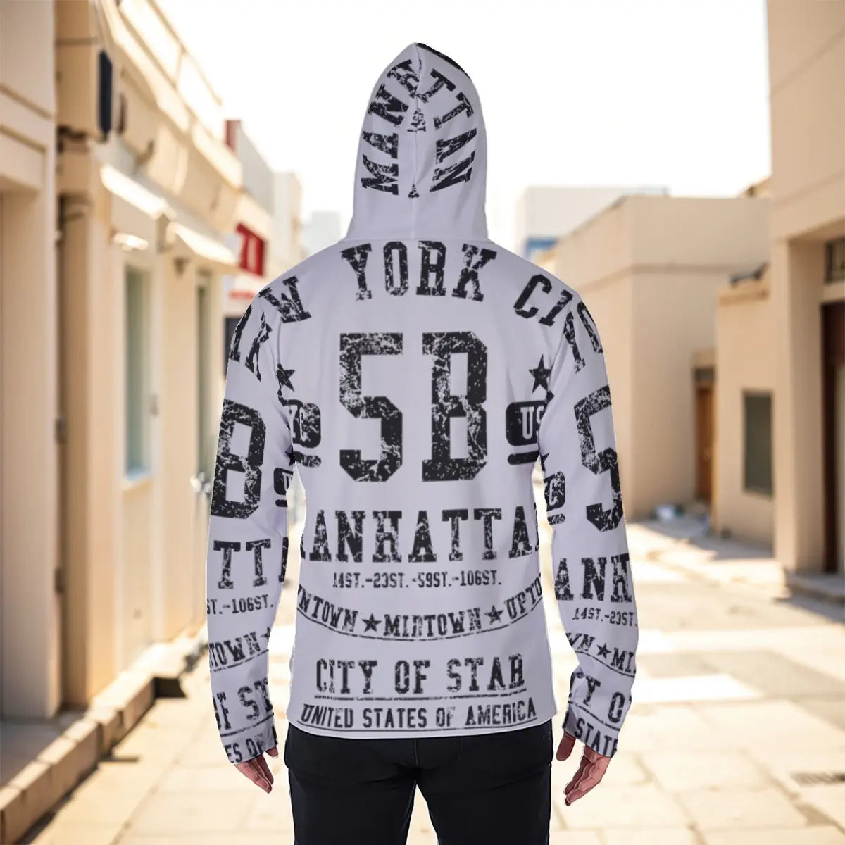 Person wearing a stylish white hoodie with New York and Manhattan prints, standing in a sunlit urban alley.