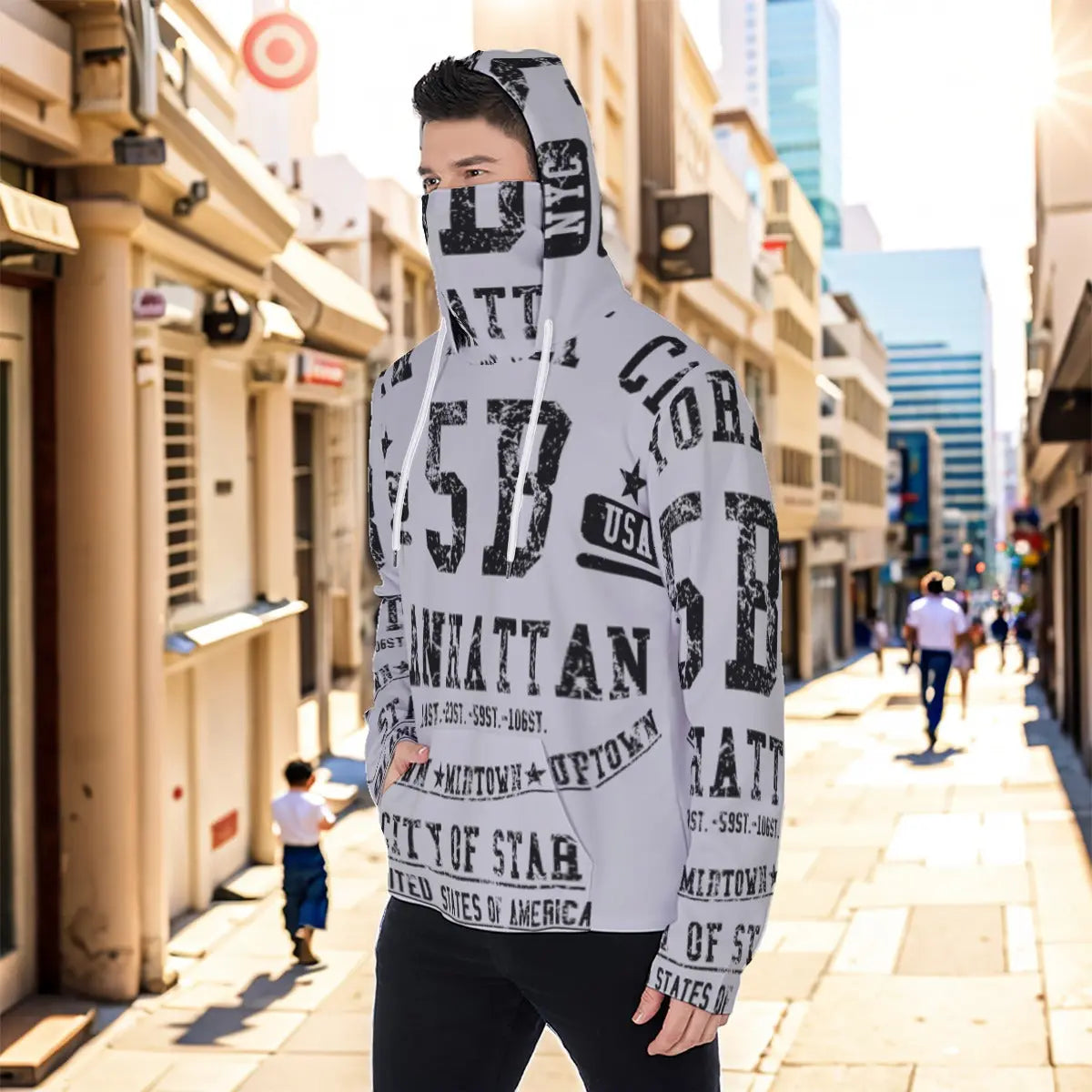Man wearing a stylish masked hoodie with graphic print, standing on a sunny urban street. Eco-friendly design with kangaroo pocket.