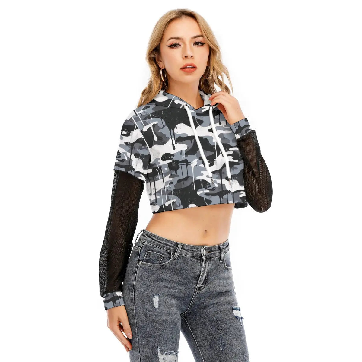 Woman wearing a layered crop top with mesh sleeves and a two-piece hoodie in camo print, paired with jeans, showcasing sporty style.